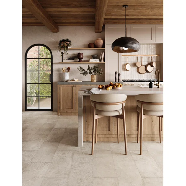 Open kitchen with oak cabinetry, arched steel door, and a pale stone island